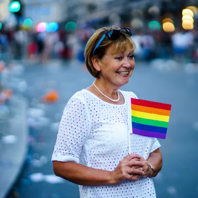 middle age woman smiling with a rainbow flag showing support for LGBTQ rights and gender transition