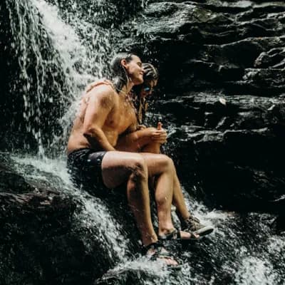 couple smiling and sitting under a waterfall